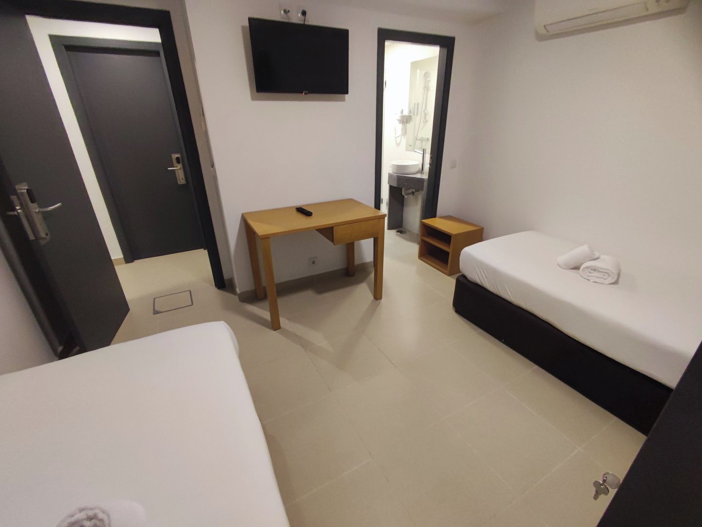 A hotel room with a bed, a desk, a TV, and a bathroom visible through an open door.