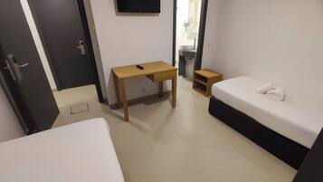 A hotel room with a bed, a desk, a TV, and a bathroom visible through an open door.