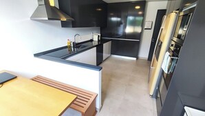Uma cozinha moderna com bancada preta, eletrodomésticos de aço inoxidável e um banco de madeira.