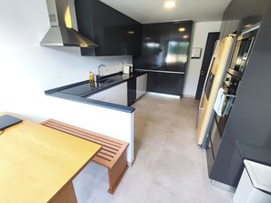A modern kitchen with a black countertop, stainless steel appliances, and a wooden bench. - Lisbon Airport GuestHouse Gal – Twin Bedroom (Lisbon)
