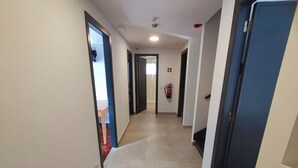 Corredor com extintor, uma caixa de emergência vermelha e uma porta que dá para outro aposento.