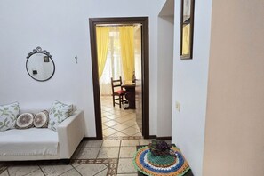 Un salon comprenant un canapé, un miroir, un centre de table en crochet et une porte donnant sur un espace repas.