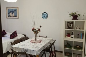 Un coin repas avec une table dressée pour deux personnes, une bibliothèque contenant divers objets et un lit avec un oreiller.