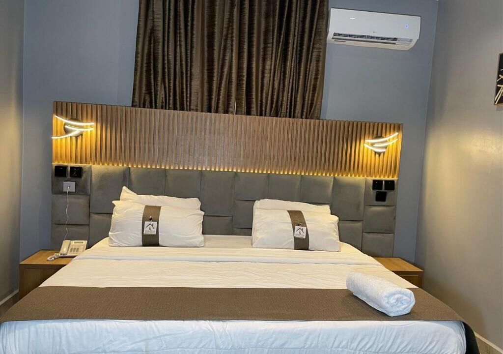 Een hotelkamer met een groot bed, hoofdbord met ingebouwde verlichting, een airconditioning en een telefoon op het nachtkastje.