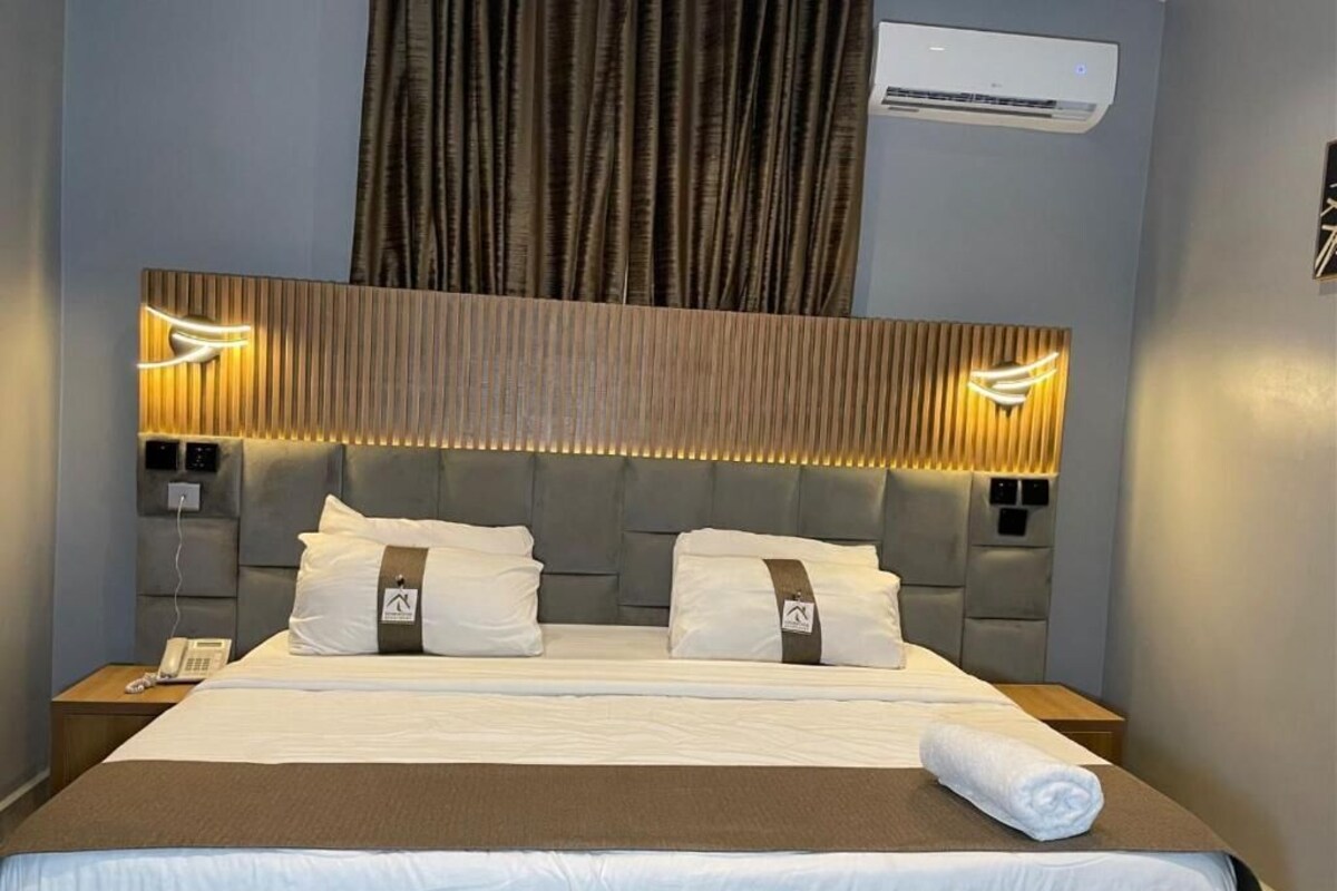 Een hotelkamer met een groot bed, hoofdbord met ingebouwde verlichting, een airconditioning en een telefoon op het nachtkastje.