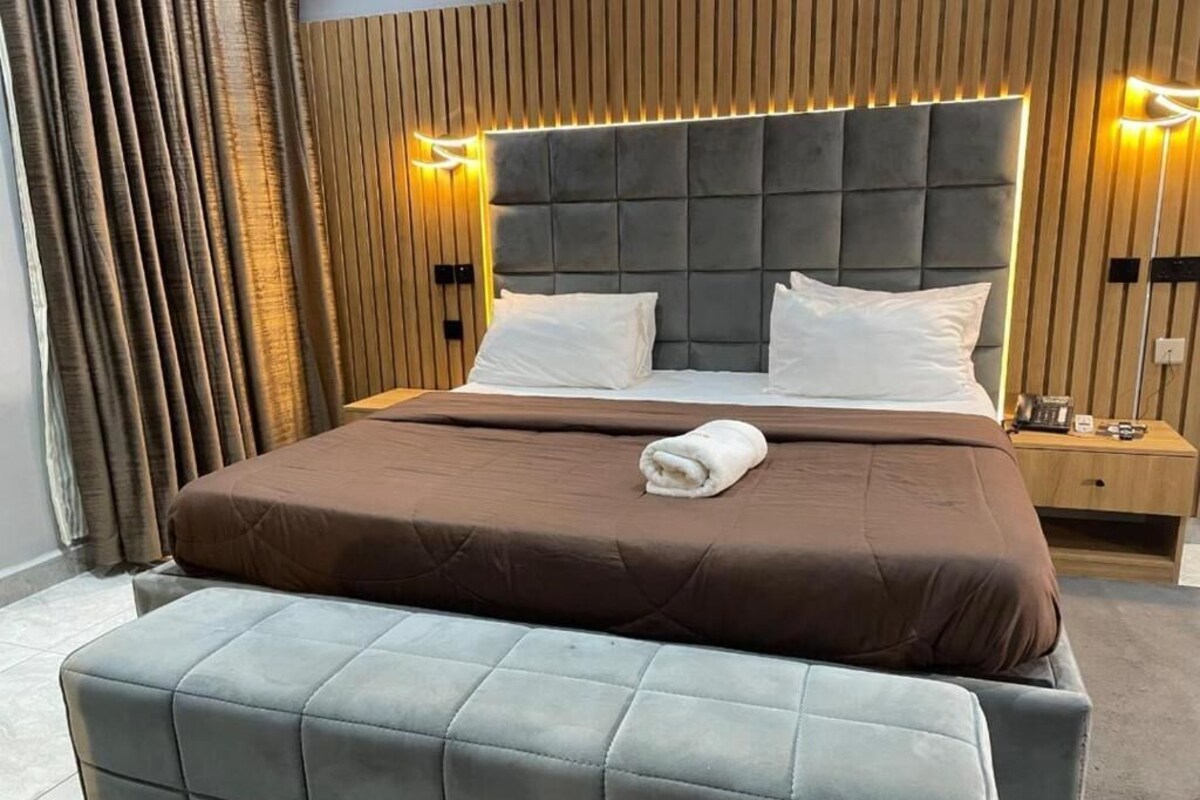 Een moderne hotelkamer met een groot bed, twee nachtkastjes en een bankje.