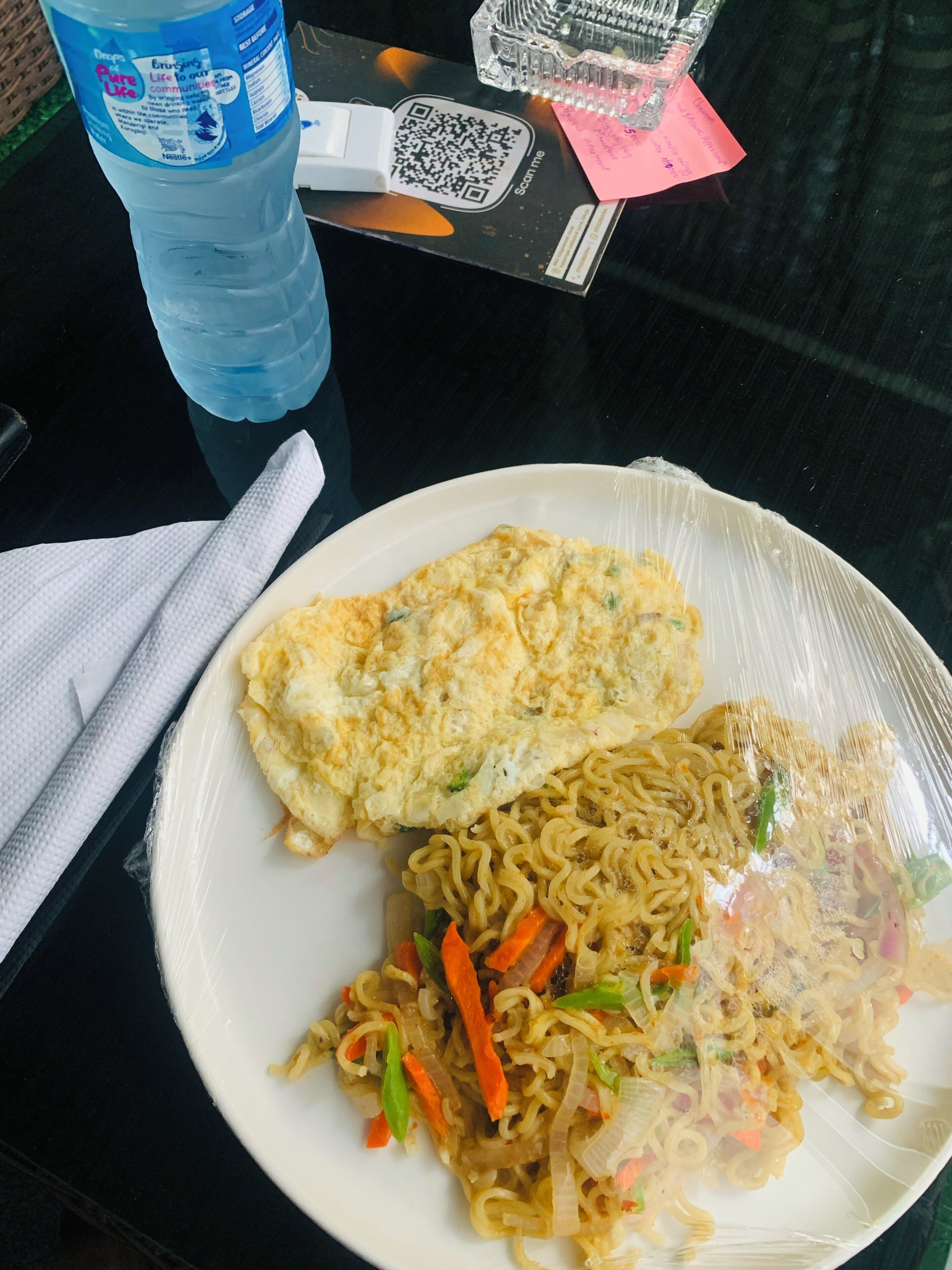A plate of food with noodles and an omelette, a water bottle, and a QR code on a table.