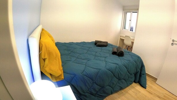 Ein gemütliches Schlafzimmer mit Bett, Stuhl, Fenster und Tür.