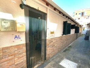 A narrow alleyway with a building featuring a metal gate, a sign reading 'AL (Alojamento Local)', and a brick wall. - Cozy one-bedr. apartment in Costa da Caparica (Costa da Caparica)