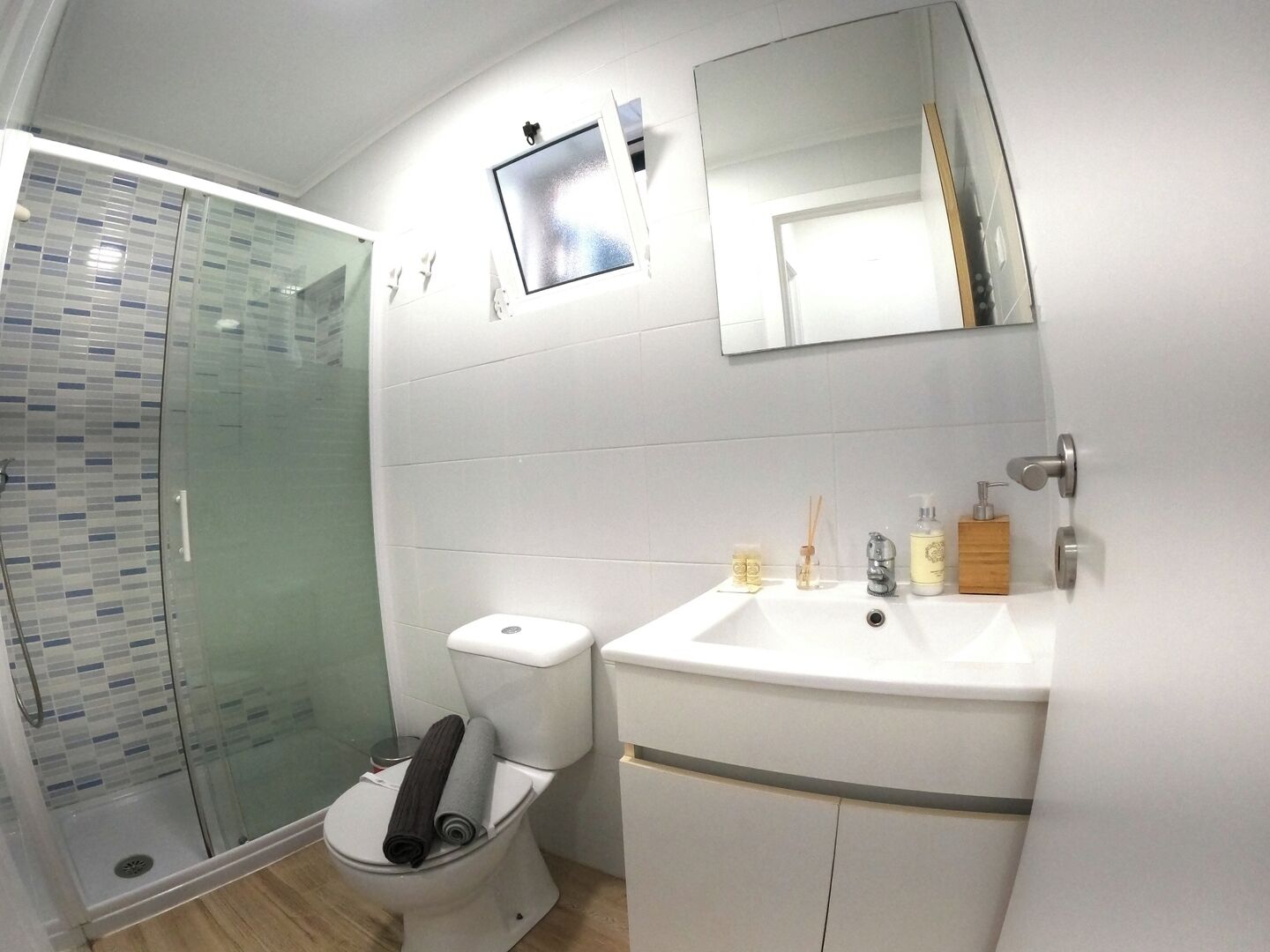 A modern bathroom with a glass shower enclosure, a toilet, a sink with toiletries, and a mirror.
