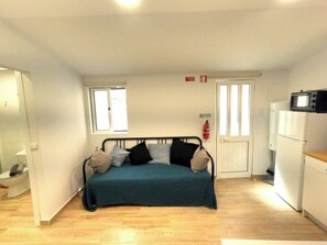 A compact room with a bed, a kitchenette, a window, and a door. - Cozy one-bedr. apartment in Costa da Caparica (Costa da Caparica)