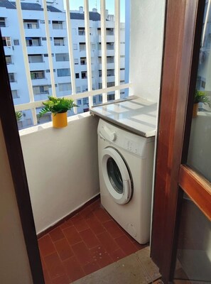 A small balcony with a washing machine, a potted plant, and a view of a residential building. - Algarve, T1 Armação de Pêra near the Beach (Armação de Pêra)