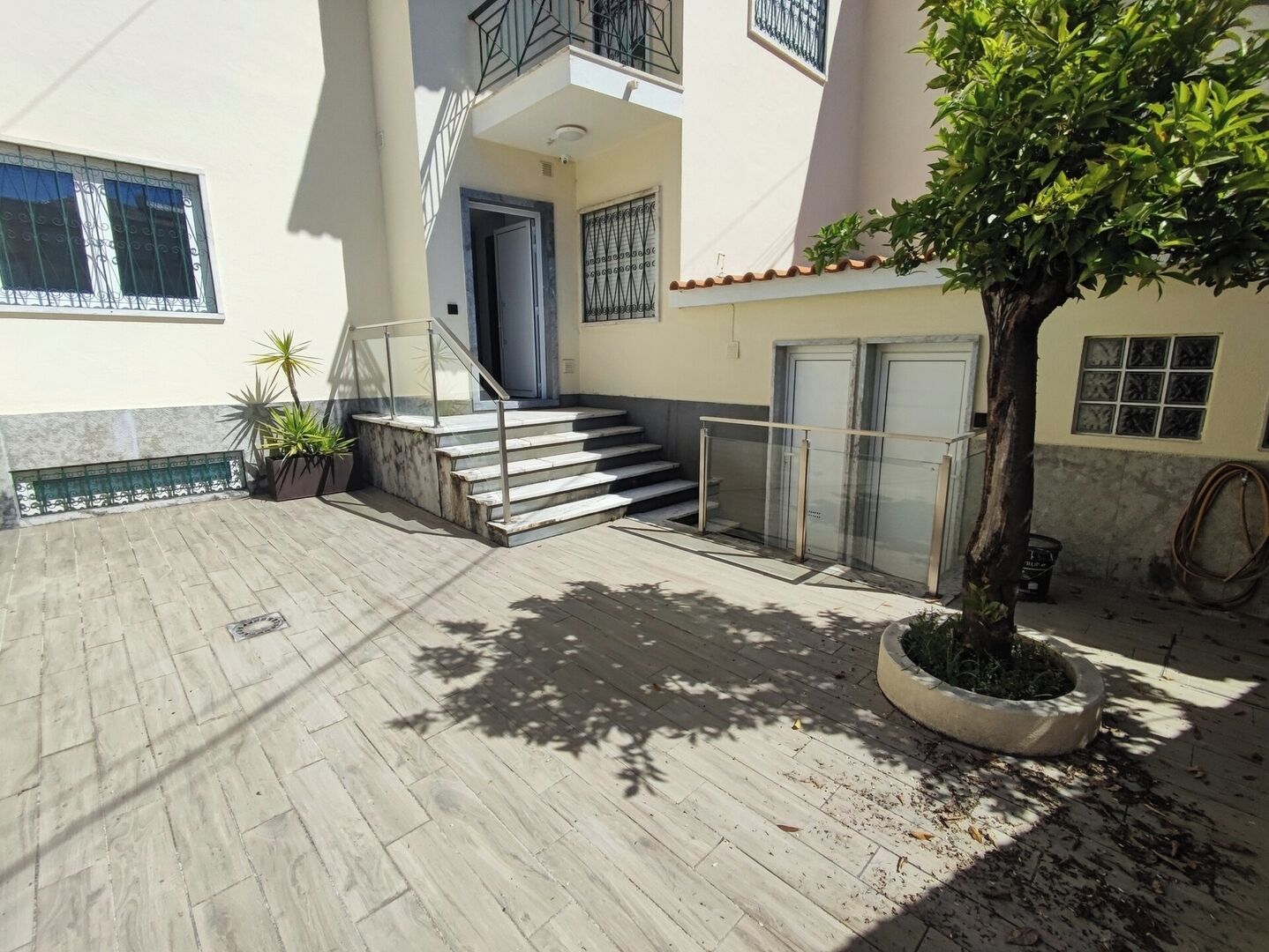 A building with a staircase leading to a door, a potted tree, and a tiled patio area.