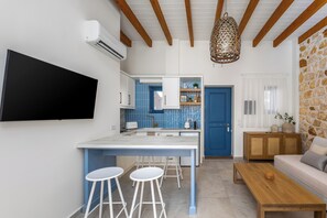 A modern kitchen with a blue door, a dining area with stools, a wooden table, and a TV mounted on the wall.