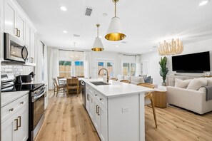 Une cuisine moderne avec des meubles blancs, un îlot central et un coin repas comprenant une table et des chaises blanches.