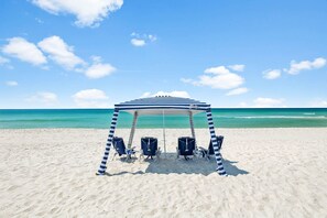 A beach with a striped canopy and four beach chairs. - Walk to the Beach | Luxe 3BR, 3BA Home with Pool + Golf Cart (Panama City Beach)