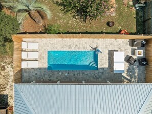 An aerial view of a rooftop swimming pool with a wooden deck, lounge chairs, and a fire pit. - Walk to the Beach | Luxe 3BR, 3BA Home with Pool + Golf Cart (Panama City Beach)