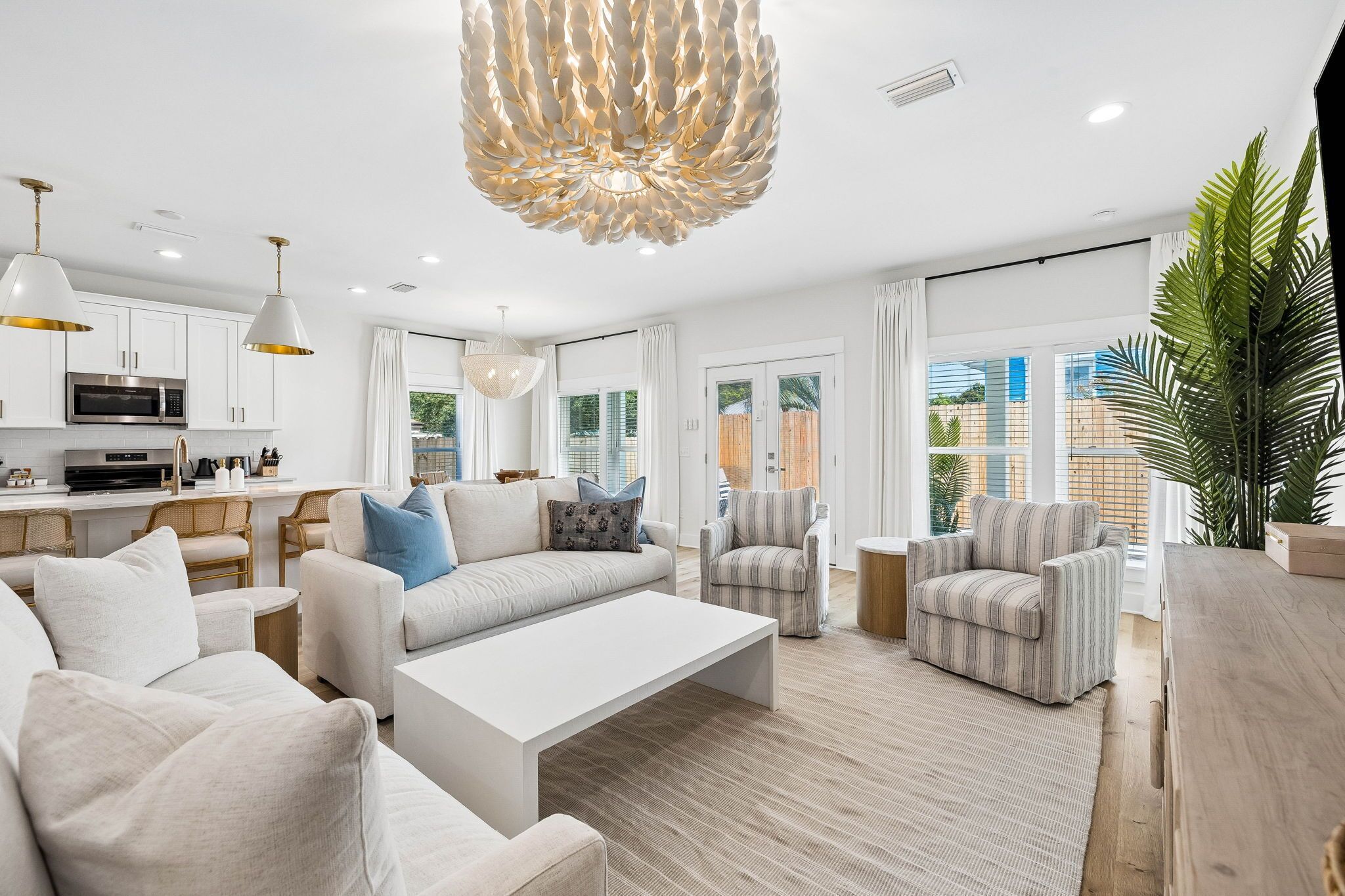 Un salon moderne avec un canapé blanc, des fauteuils, une table basse et un coin repas, la cuisine étant visible au fond.