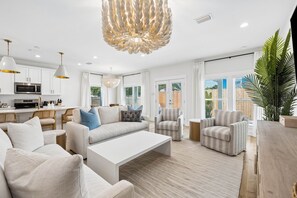 A modern living room with a white sofa, armchairs, a coffee table, and a dining area with a kitchen in the background. - Walk to the Beach | Luxe 3BR, 3BA Home with Pool + Golf Cart (Panama City Beach)