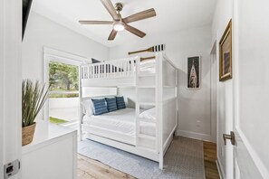 Un lit superposé avec un ventilateur de plafond, une plante en pot et un tableau encadré accroché au mur.