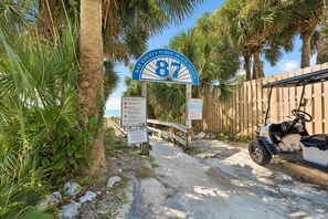Un panneau indiquant l’entrée de la plage, avec un drapeau d’avertissement, un véhicule de type voiturette de golf et une clôture en bois.