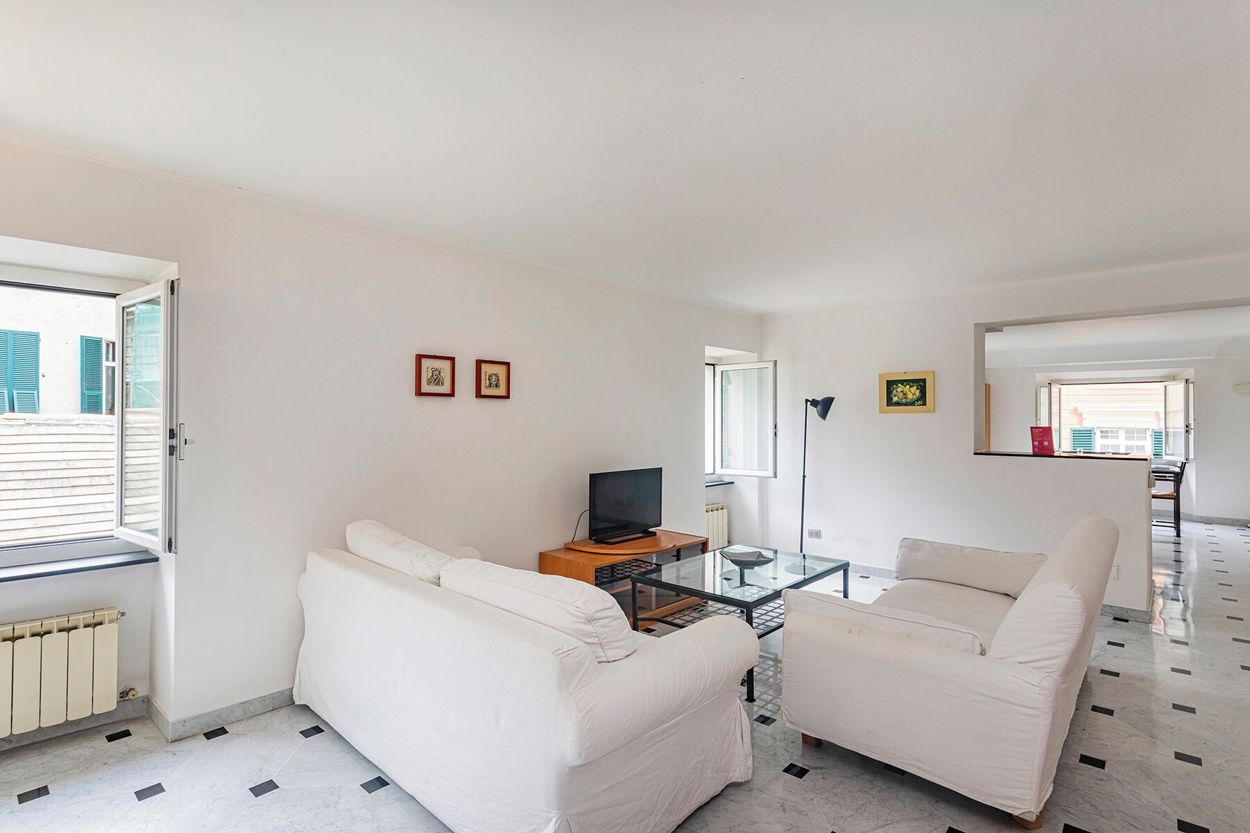 Una sala de estar con un sofá, una mesa de centro de vidrio, un televisor y un radiador.