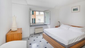 Makuuhuoneessa on sänky, yöpöytä, lamppu, ikkuna, josta on näkymä rakennuksiin, ja patteri.