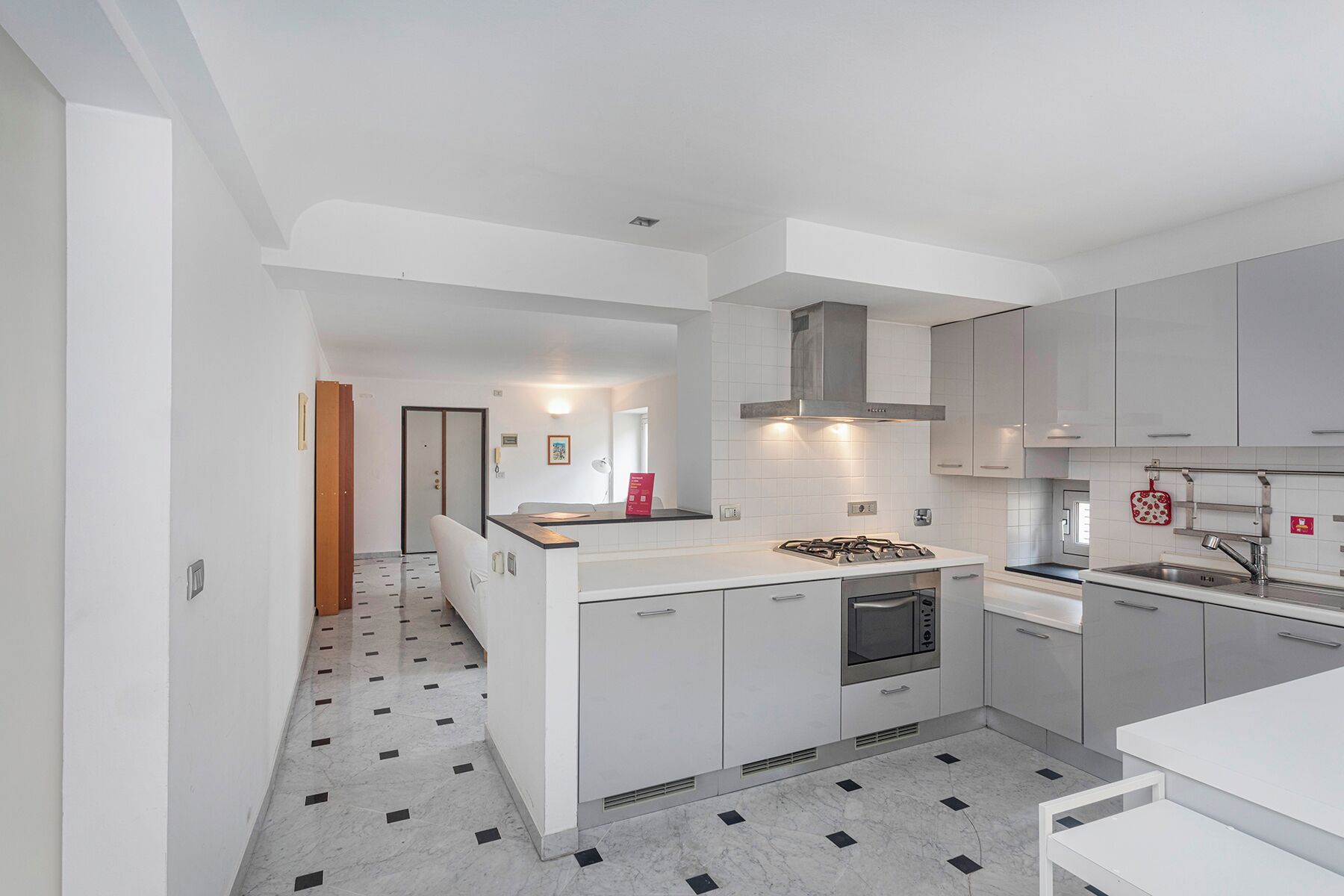 Una cocina moderna con armarios blancos, una isla central, horno integrado y campana extractora de acero inoxidable.