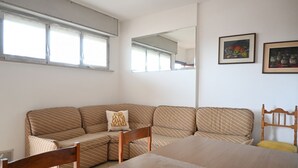Una habitación con sofá, cama, mesa de comedor, espejo y dos cuadros en la pared.