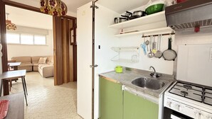 Cocina compacta con estufa a gas, pileta y diferentes utensilios de cocina.