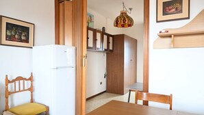 Una habitación con una mesa de comedor de madera, un refrigerador blanco, un armario de madera y una puerta que da a otra estancia.