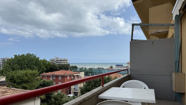 Un balcón con mesa y sillas, con vista a una playa y edificios.