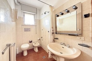 Et badeværelse med toilet, bidet, vask, spejl og brusebad.