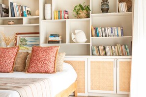 Ein Schlafzimmer mit Bett, Kissen, einem Bücherregal und einer Dekovase.