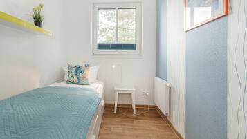 Ein Schlafzimmer mit Bett, Nachttisch, Fenster, Heizkörper und einer Wand mit einem Bilderrahmen.