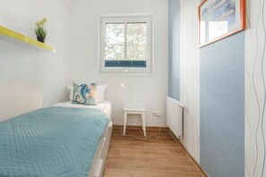A bedroom with a bed, a bedside table, a window, a radiator, and a wall with a picture frame.