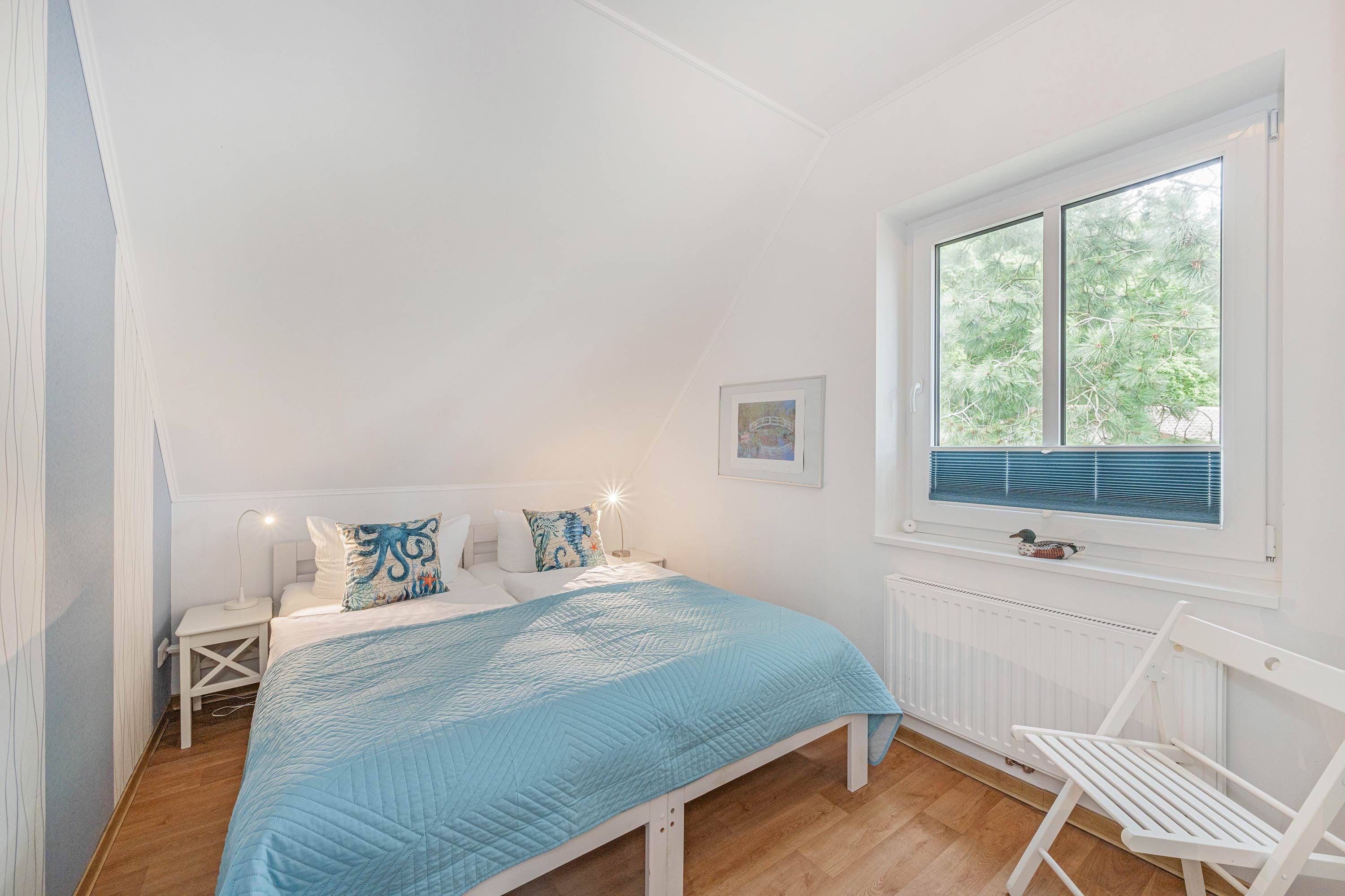 Ein Schlafzimmer mit einem Bett, einem Nachttisch, einem Schreibtisch, einem Stuhl, einem Fenster mit Jalousien und einer Heizung.