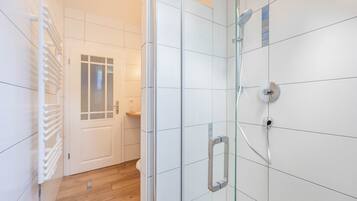 A modern bathroom with white tiles, a glass shower enclosure, and a wooden floor.