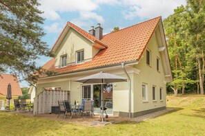 A two-story house with a red-tiled roof, a covered patio with outdoor furniture, and a fenced backyard.