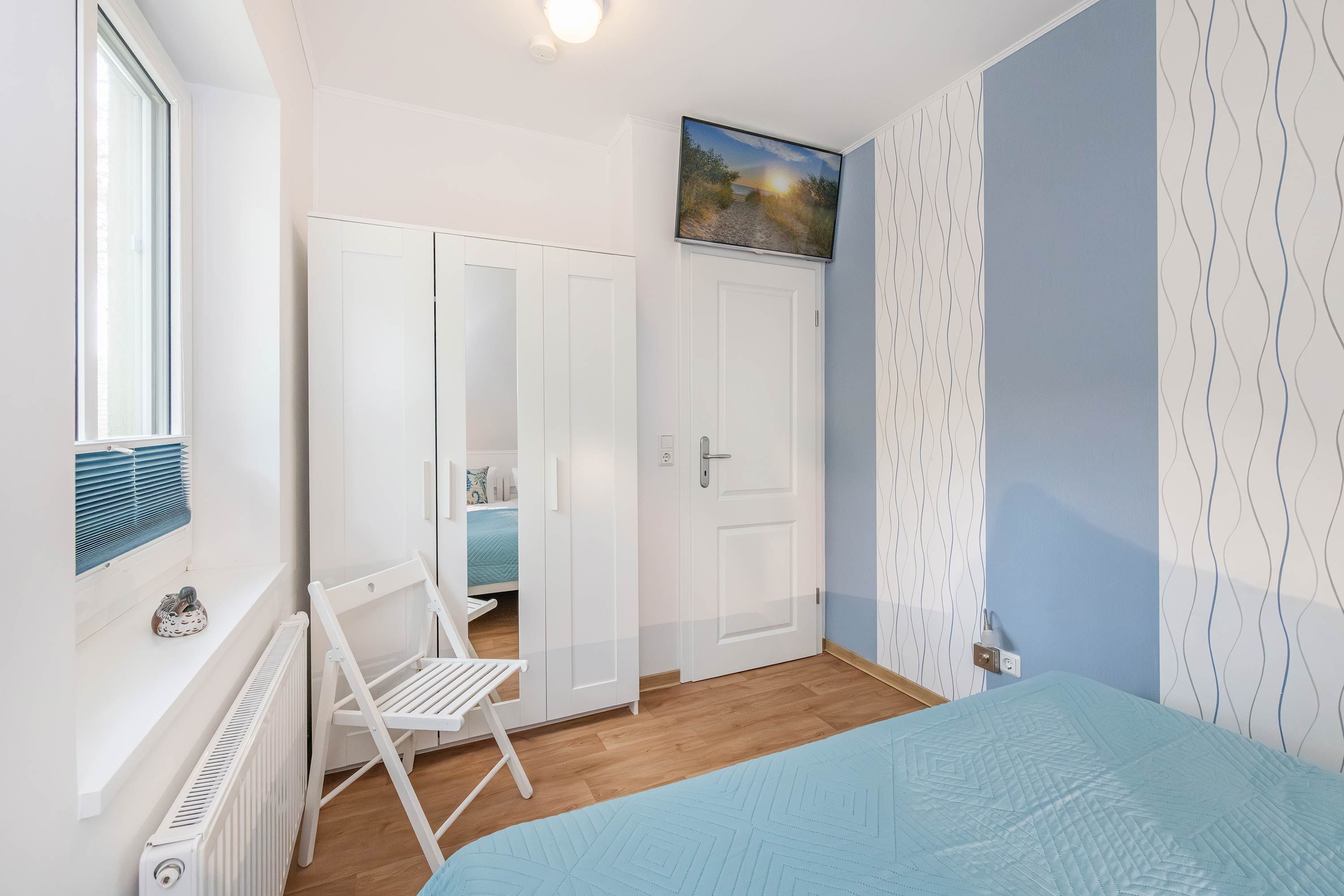 Een slaapkamer met een bed, een stoel, een kledingkast, een radiator en een schilderij aan de muur.