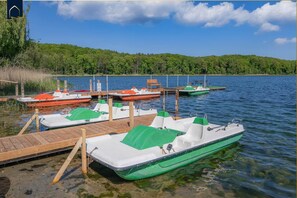 A dock with several small boats, a wooden pier, and a forested shoreline. - Quiet vacation home in Korswandt surrounded by nature—with a garden, fireplace, and infrared sauna (Korswandt)