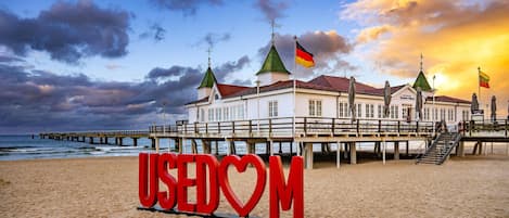 A beach with a large red sign reading 'USEDOM' and a building with multiple flags.