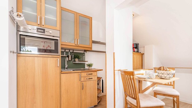 Een functionele keuken met houten kastjes, een inbouwoven en een eethoek met een tafel en stoelen.