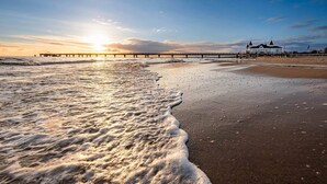 Een strand met golven, een steiger en een gebouw met een witte gevel.