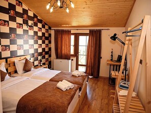 Habitación de hotel con dos camas, techo de madera, pared a cuadros, ventana con cortinas, escritorio con una computadora portátil y una silla.