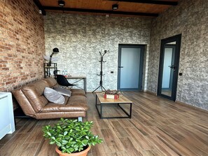 Ein gemütliches Zimmer mit Backsteinwand, Ledersofa, kleinem Tisch, Topfpflanze und einer Tür.