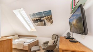 Ein kleines Zimmer mit Bett, Schreibtisch, Stuhl und einem großen Fernseher.