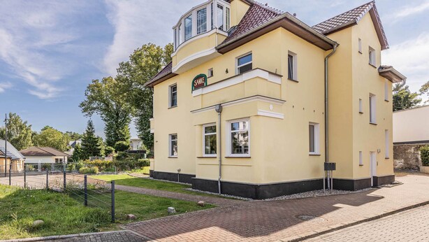 Ein zweistöckiges Gebäude mit einer gelben Fassade und einem Schild mit der Aufschrift 'Sanke'.