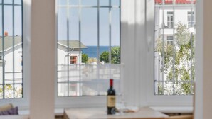 Ein Zimmer mit großem Fenster, einer Weinflasche und Blick auf Gebäude und Bäume.