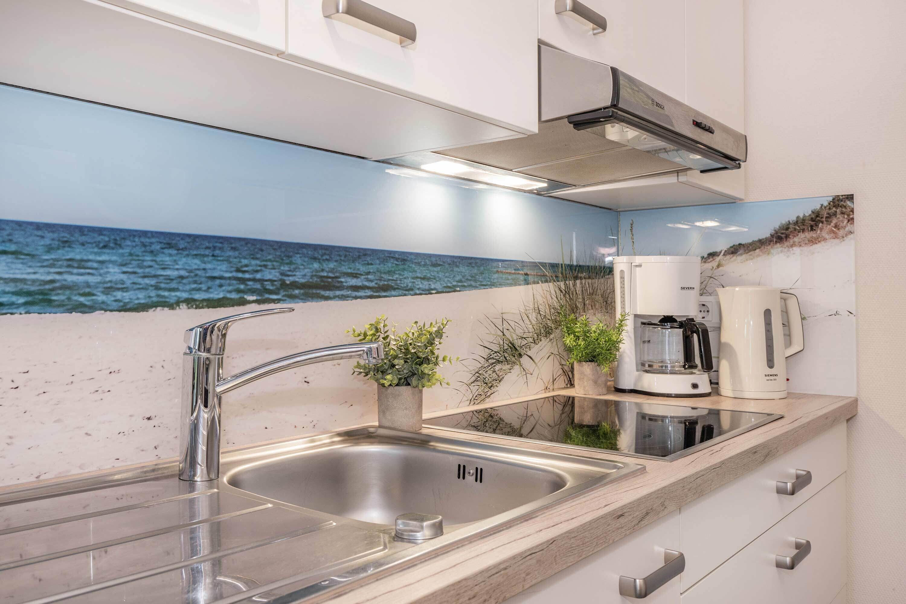 A kitchen with a stainless steel sink, a coffee maker, and a view of the ocean through a large window.
